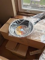 Photo of a single 12-inch frying pan with a black handle and Teflon coating on top of sealed boxes.
