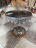 Full view of the pedestal cake stand showing polished stainless steel round top and decorative metal rim embossed with fruit motifs.