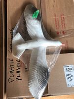 Top view of one plastic sea gull figurine with white body, gray wing tips, and red beak wrapped in plastic on top of a cardboard box labeled 'plastic sea gulls'.