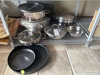 Eight stainless steel pots and two baking pans displayed on wire shelf