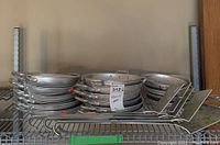 Shelf with nine stacked aluminum sauce pans and five aluminum spatulas laid next to them.