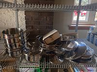 Stack of stainless steel sauce pots and lids on shelving rack, showing multiple sizes and lids