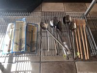Photo showing the full set of utensils including packaged cheese forks, stainless steel spoons, and wooden forks arranged on wire rack