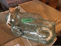 Side view of a pressed glass storage jar shaped like a car with cork top and metal clasp, resting on cardboard boxes