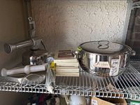 Full view of tomato press, candle boxes stacked, stainless steel stock pot with glass lid and manometer on a wire shelf.