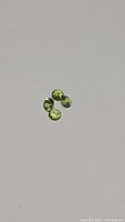 Four diamond cut apple green peridot gemstones displayed individually showing bright green color and cut pattern.