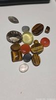 Photo showing 17 loose natural gemstones arranged on white surface with digital scale visible in background.