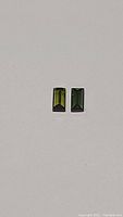 Pair of small rectangular baguette green tourmaline gemstones shown side by side on white background.