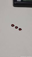 Three natural cherry red garnet gemstones, pear shaped, laid in a row on a white surface.