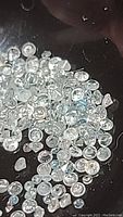 Close-up image of many small zircon gemstones showing white and light teal colors, faceted and translucent.
