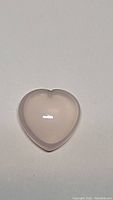 Close-up photo of the hand carved heart-shaped rose quartz gemstone on a neutral background showing the smooth, polished pink surface.