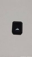 Close-up photo of the 15 carat natural jet black onyx gemstone showing the emerald cut top surface and polished facets.