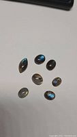 Photo of seven labradorite cabochon stones on white surface showing blue and golden flash colors.