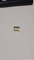 Photo of a loose rectangular emerald cut lemon citrine gemstone on a white surface showing its color and cut.