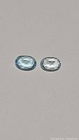 Pair of oval cut natural sky blue topaz gemstones placed side by side on neutral background showing matching color and clarity.