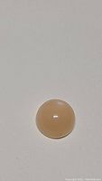 Close-up of a smooth, round peach moonstone cabochon on a neutral background, showing polish and color.