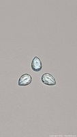Three pear cut sky blue topaz gemstones arranged on a light surface, showing their shape and clarity.