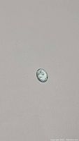 Photo showing the oval cut aquamarine gemstone with visible facets and light reflection against a plain background.