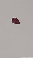 Pear cut pink orange tourmaline gemstone with visible inclusions on a plain white surface.