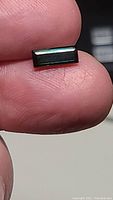 Close-up image of rectangular blue-green Paraiba tourmaline gemstone held between fingers showing its color and cut.