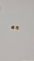 Pair of small round yellow faceted sphene gemstones showing brilliance and rainbow luster on white background.