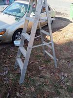 Side view of 5 foot aluminum step ladder on ground, leaning slightly, showing five steps and supporting braces.