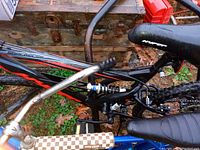 Side angle of hybrid bicycle showing bent front tire, frame, rear suspension, seat, and handlebars.