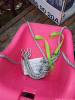 Pink plastic children's swing with coiled rope and metal hooks on wooden pallet, showing dirt and need for cleaning.