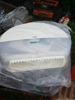 White plastic double roll toilet paper dispenser partially wrapped in plastic, showing serrated tear edge and Tork brand label.