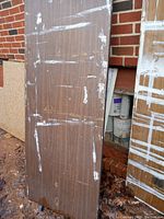 Photo showing wooden foldable table top with paint marks and scuffs leaning against brick wall.
