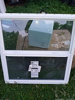 White vinyl window with two glass panes, one large top pane and smaller bottom pane, shown against a background of grass and cardboard.