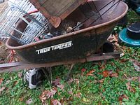 Close-up of rusty True Temper metal wheelbarrow with wooden handles and filled with miscellaneous items not included in lot.