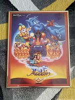 Full view of framed Aladdin movie poster featuring Genie, Aladdin, Jasmine, and other characters from the film.