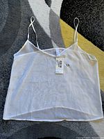 White sheer camisole top laid flat on floor showing entire top and straps