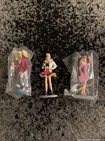 Front view of three Barbie PVC figures, two bagged and one unbagged, showing their outfits and poses