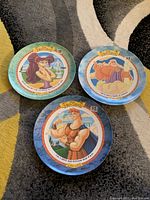 Three Disney Hercules McDonald's collector plates from the 1990s displayed on carpet, showing character illustrations and decorative borders.
