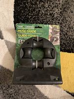 Front view of the black hose guide attached to original packaging with visible mounting holes and instructions.