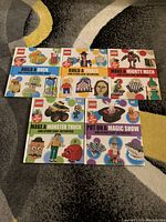 Front view of 5 LEGO building activity books arranged in two rows on a carpet showing colorful themed covers.