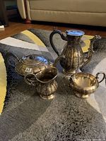 Full view of the 4-piece antique E.P. copper tea set showing the coffee pot, teapot, creamer, and sugar bowl on a carpeted floor.