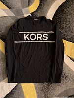 Full view of black long sleeve shirt showing front with KORS print.