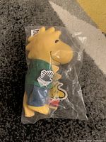 Side view of the Woodstock plush figure sealed in clear plastic showing the full figure and tags, shape and attire visible.