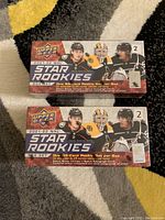 Top front view of two sealed Upper Deck 2021-22 NHL Star Rookies hockey card box sets, showing branding, player images, and 25 card rookie set info. One box has a dent on top right corner.