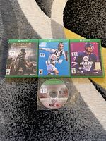 Front side of four Xbox One game cases and one loose disc: Dead Rising 4, FIFA 19, NHL 20 cases, and NHL 16 disc, laid on a patterned carpet.