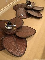 Two large ceiling fans placed on the floor showing their wide, leaf-shaped woven blades and central housing units.