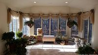 Sunroom windows with three curtain rods and attached beige striped curtains with valances and decorative floral end brackets