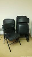 Eleven black folding chairs stacked together, one unfolded to show seat and backrest