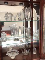 Glass cabinet with clear cut glass vases, bowls, and dishes, showing various shapes and intricate cuts in glass.