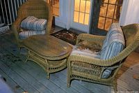 Pair of rattan chairs with striped cushions and oval coffee table on deck showing wear and dirt.
