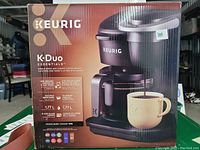 Boxed Keurig K-Duo Essentials coffee maker, showing model name, features, and image of the coffee maker brewing into a cup.