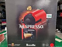 Boxed Breville Nespresso Inissia espresso machine, red, showing front packaging with cup of espresso and product image.